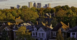 An image of a neighborhood with trees and a city skyline in the background